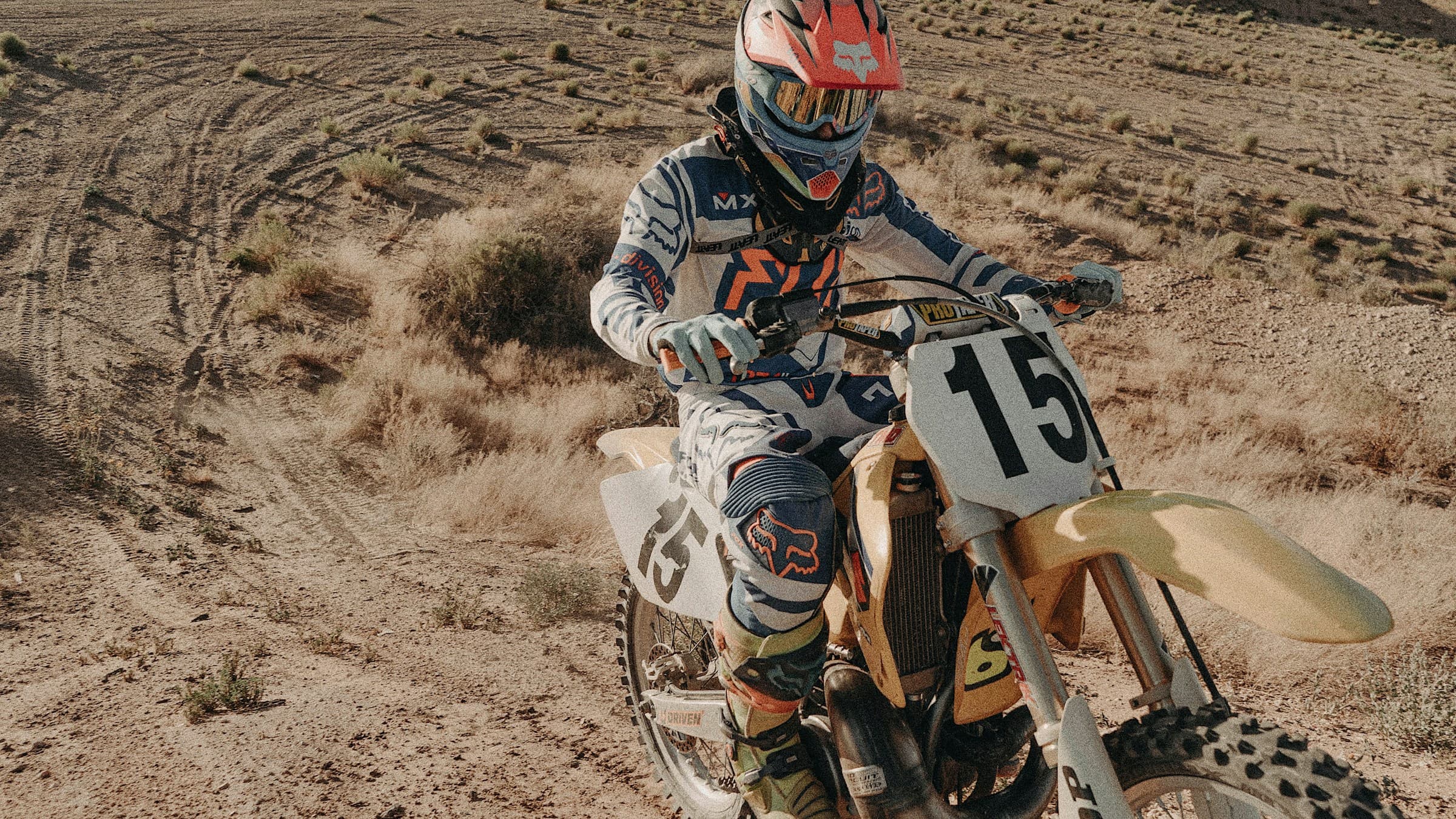 Enduro rider on a yellow dirt bike crossing arid hill trails at golden hour