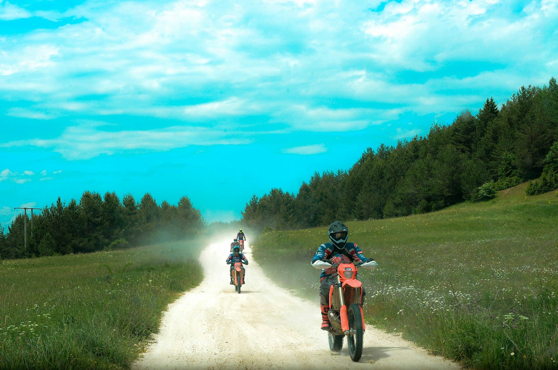 Group of enduro riders on orange dirt bikes rolling down a dusty mountain trail.
