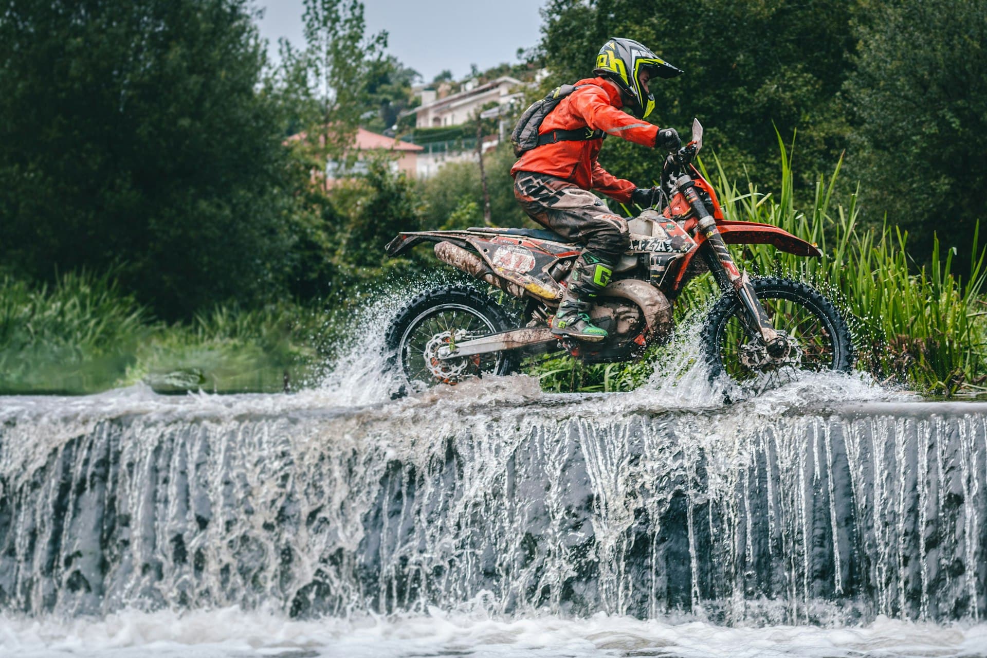Enduro rider crossing a rocky stream on a muddy dirt bike through green Algarve terrain