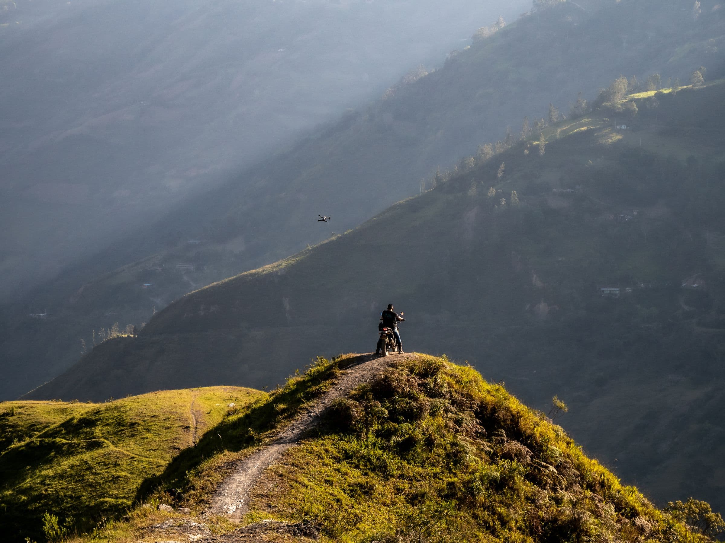 Motorcyclist paused on a grassy mountain ridge overlooking a misty valley at golden hour