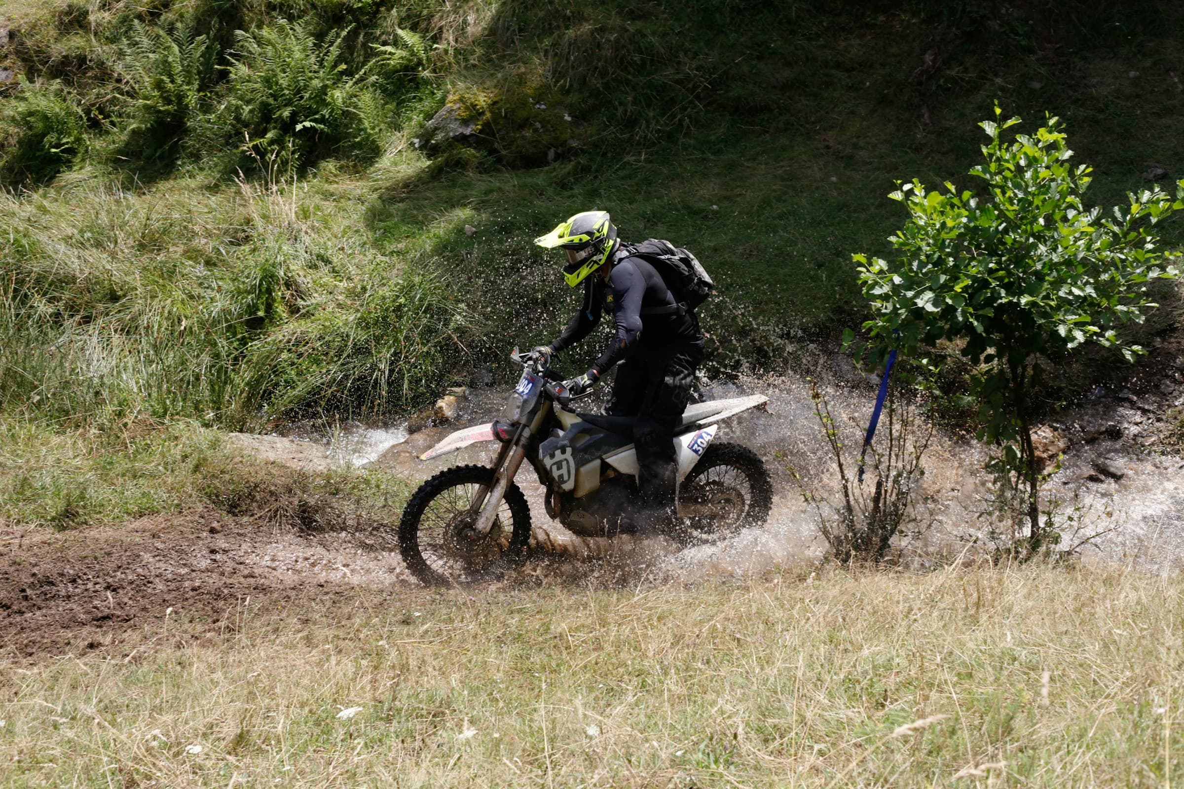 Enduro rider on a dirt bike splashing through a muddy trail stream